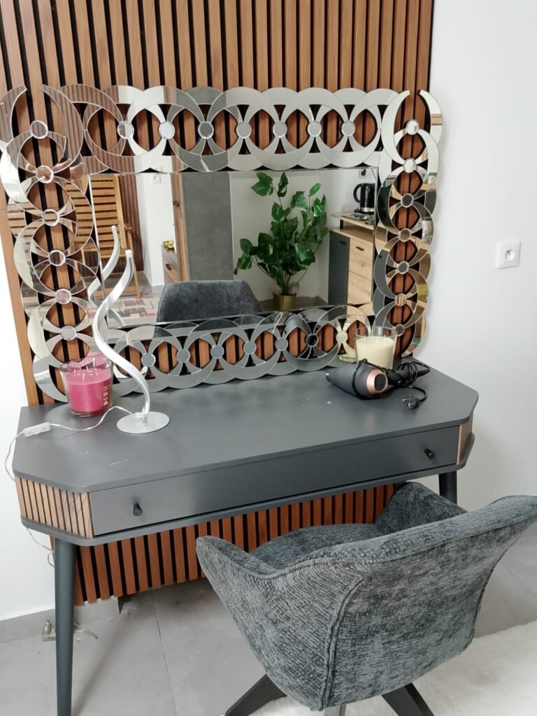 Le miroir géométrique de la coiffeuse, devant le mur en tasseaux de bois.